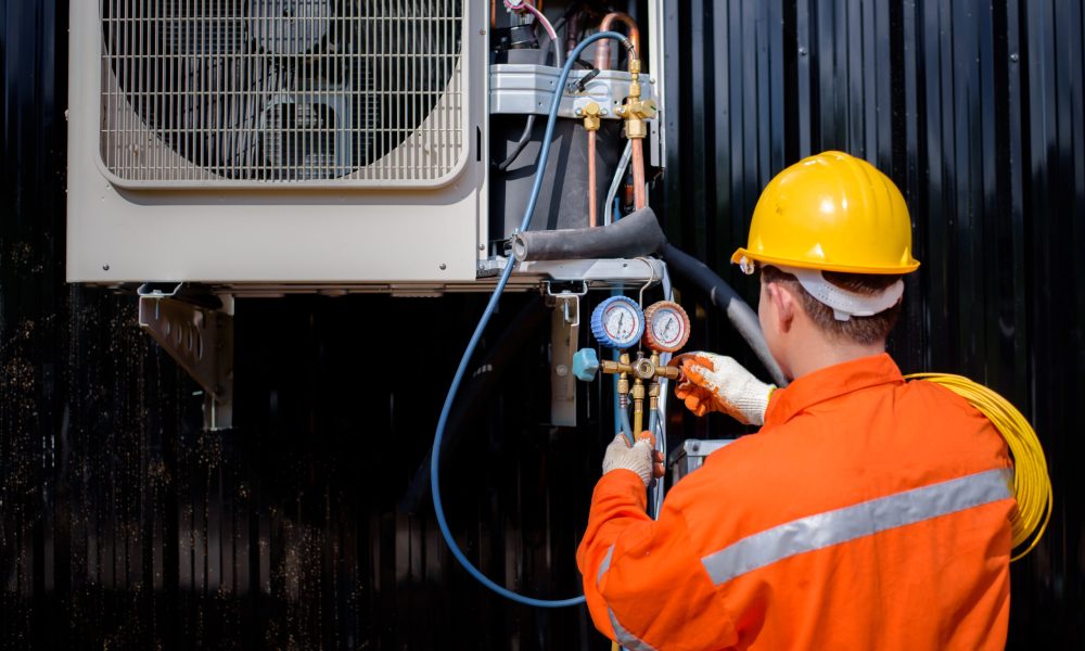 An Asian male air technician is checking the compressor and filling it up for home and building air conditioners.