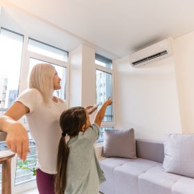 Happy family under air conditioner, mom holding remote control switch on conditioning in living room adjust comfort temperature for daughter, climate system at modern home